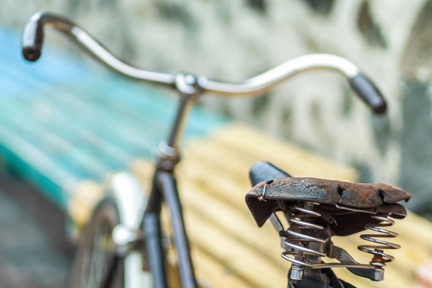 Ένα παλιό κάθισμα ποδηλάτου με ένα ελατήριο αμορτισέρ. Εκλεκτής ποιότητας ποδηλάτων για το ιστορικό πέτρινο τοίχο. - Φωτογραφία, εικόνα