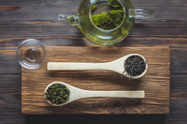 Traditional Chinese green tea different fermentation wooden culinary spoons teapot with fresh brewed leaves on dark table low key food concept top view Wabi Sabi lifestyle. - Photo, Image