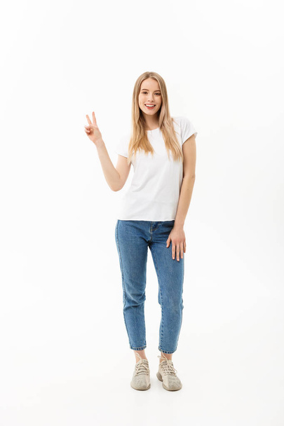 立っている、白い背景に分離された 2 つの手で平和のジェスチャーを示す幸せな若い女性の完全な長さの肖像画 - 写真・画像