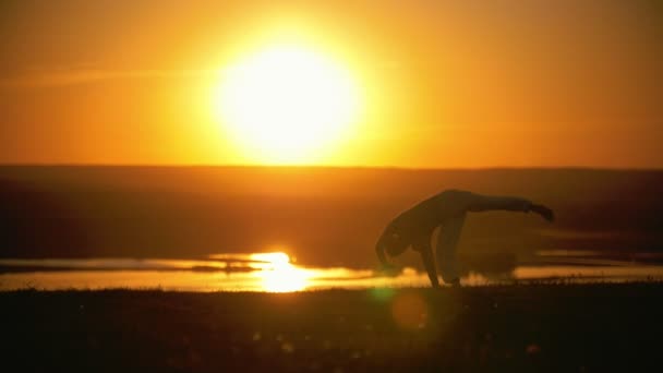 Egy ember végez akrobatikus mutatványokat, bukfenc, narancssárga naplemente, lassú mozgás - Felvétel, videó