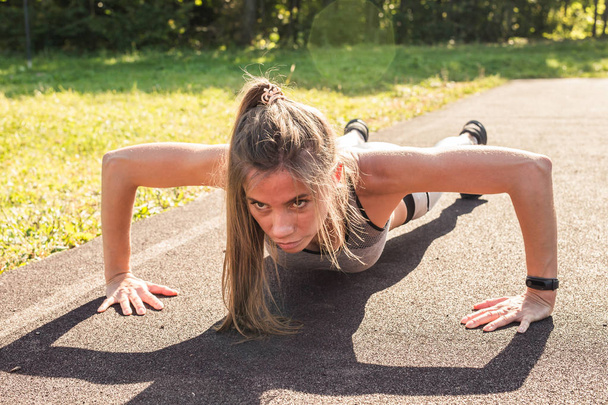 Γυμναστήριο γυναίκα κάνει push-ups κατά τη διάρκεια της προπόνηση προπόνηση σε εξωτερικούς χώρους σταυρό. Όμορφη νεαρή και fit fitness sport μοντέλο κατάρτιση έξω στο πάρκο - Φωτογραφία, εικόνα