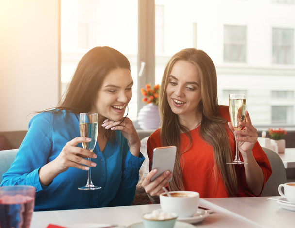 Happy female frinds with champagne and smartphone at cafe - Foto, afbeelding