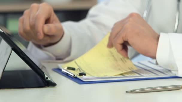Experienced physician looking at registration form, prescribing treatment online - Filmagem, Vídeo
