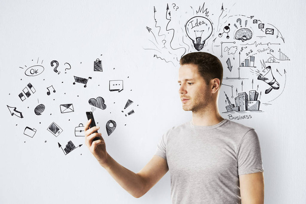 Side portrait of attractive young man using smartphone on concrete wall background with creative business sketch. Technology, communication and plan concept  - Photo, Image