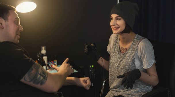 Tattooist wesoły kobieta robi tatuaż z maszynka do tatuażu na męskie ramię. Niezwykłe kobiece zawód, miejsce - Zdjęcie, obraz
