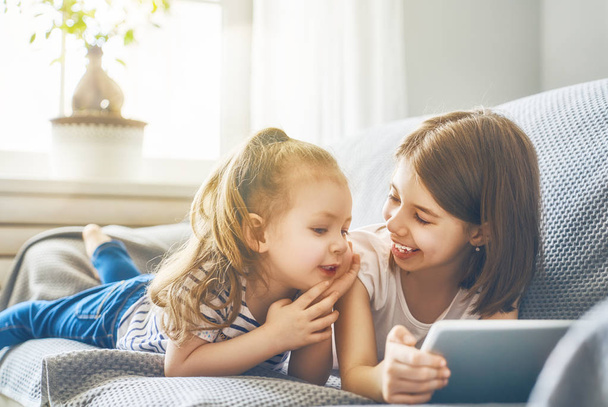 Cute little children are playing with tablet. Happy girls at home. Funny lovely sisters are having fun in kids room.  - Φωτογραφία, εικόνα