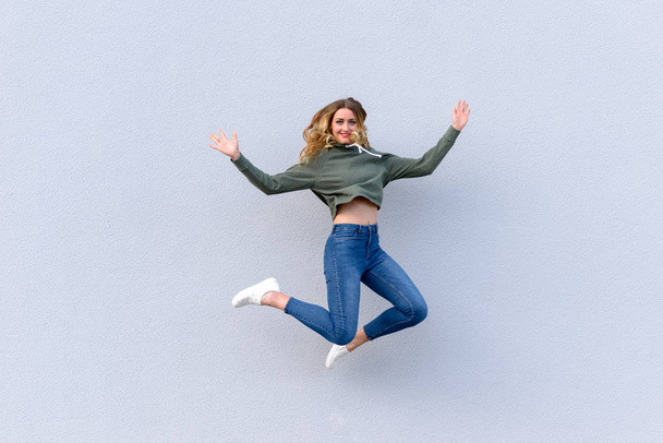 Portret van vrolijke jongedame in spijkerbroek springen in de lucht tegen de witte achtergrond - Foto, afbeelding