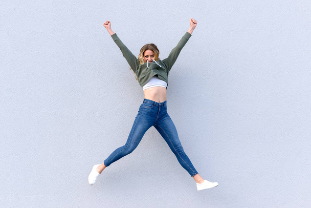 白い背景に対して空気に飛び込むジーンズの若い陽気な女性の肖像画 - 写真・画像