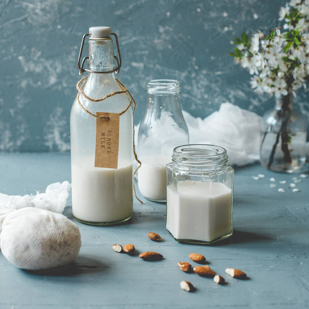 Vegan non-dairy almond milk in glass bottles on wooden background. - Fotografie, Obrázek