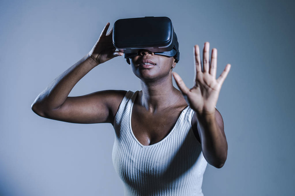 young attractive curious black afro american woman wearing VR 3d vision goggles enjoying amazing experience playing and having fun in virtual reality video game on isolated background - Фото, изображение