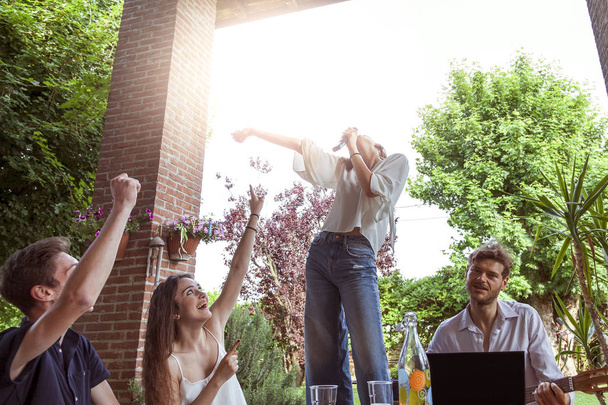 group of young friends having fun singing a song in the courtyard of a country house - 写真・画像