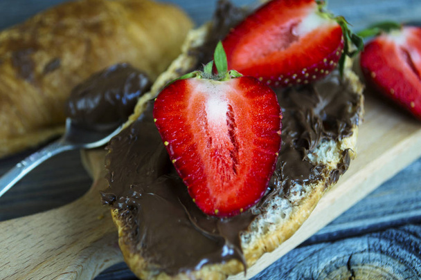 croissant with chocolate pasta and strawberries on an old wooden background - Fotoğraf, Görsel