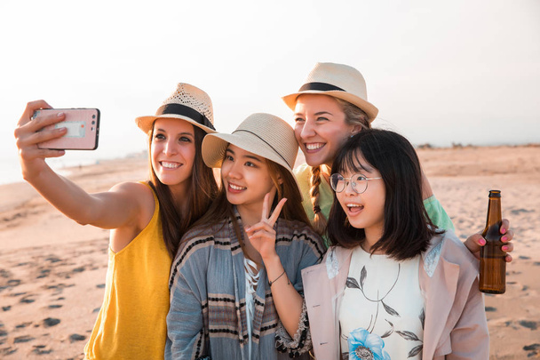 Happy multiracial young women making a selfie at the beach while they are in a summer party. Friends and holiday concept - Photo, Image
