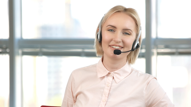 Mature female employee is working in call center. Portrait of smiling woman with microphone is talking. - Felvétel, videó