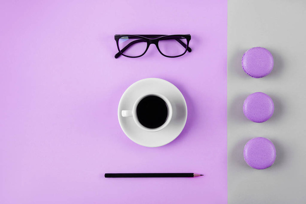 Coffee, macaron, clean notebook, eyeglasses and flower on violet table from above. Female working desk. Flat lay style. - Photo, Image