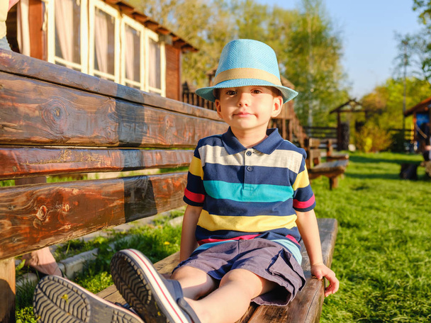 Smiling child sitting on a park bench with green meadow on the background - Fotografie, Obrázek