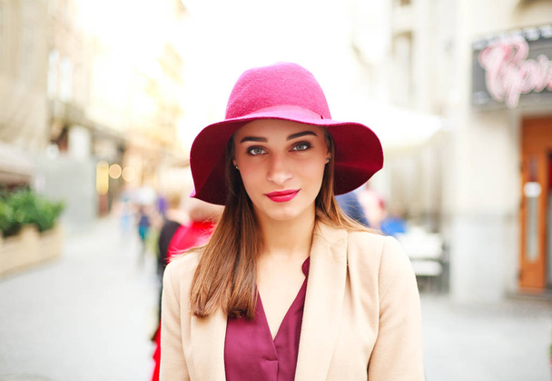 Cute smiling woman in a coat and purple hat on a street tourist town - 写真・画像