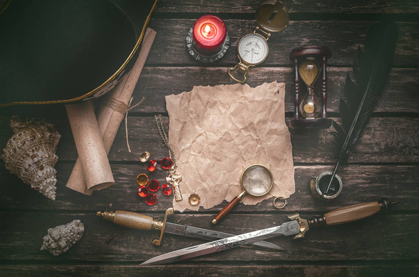 Pirate captain table with crumpled paper page with copy space for treasure map, golden compass, sand watch, scrolls,gemstones, seashell and dagger. - Photo, Image