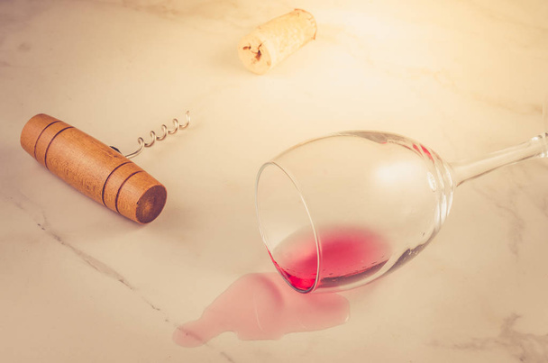 turned wine glass and corkscrew on marble background/poured red wine glass and wooden corkscrew on marble background.  - Fotó, kép