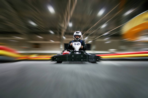 De man in een helm in de go-kart beweegt op een karting-circuit - Foto, afbeelding