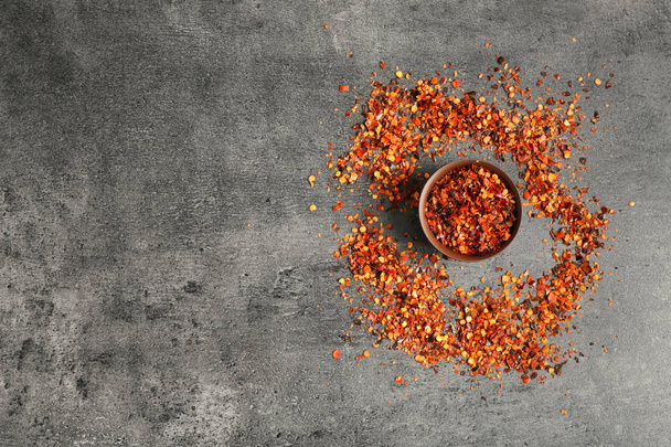 Bowl with chili pepper flakes on grey background, top view - 写真・画像