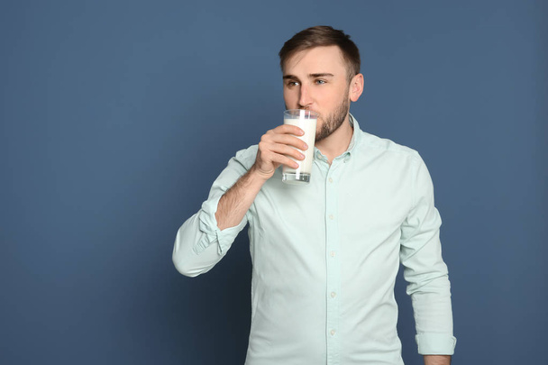 Young man drinking tasty milk on color background - Foto, afbeelding