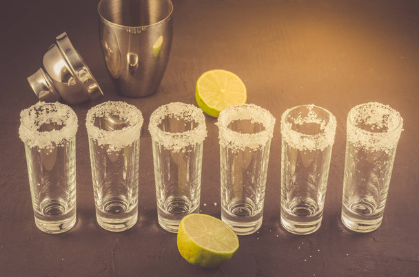 shots of tequila and pieces of lime and shaker/shots of tequila and pieces of lime and shaker on a stone background.  - Photo, image