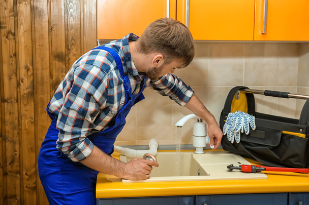 Professional plumber in uniform fixing kitchen sink - Photo, image