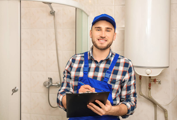 Professional plumber in uniform with clipboard indoors - Fotografie, Obrázek
