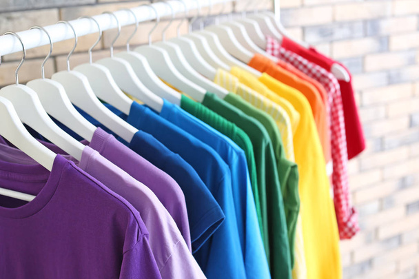 Rack with rainbow clothes on brick wall background - Фото, изображение