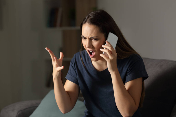 Angry customer claiming on the phone sitting on a couch in the living room at home - Фото, изображение