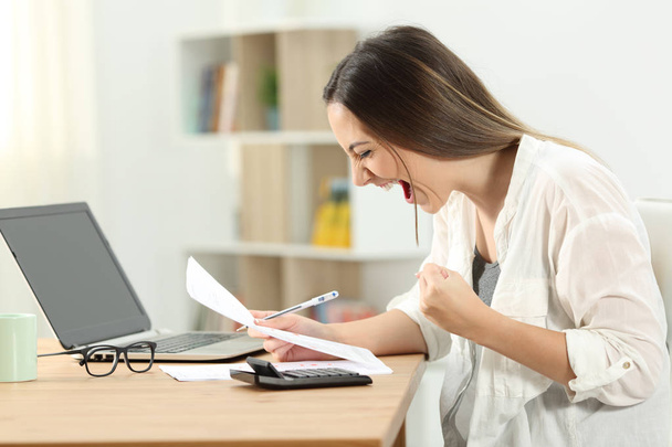Excited woman checking bank statement on a desk at home - Фото, изображение