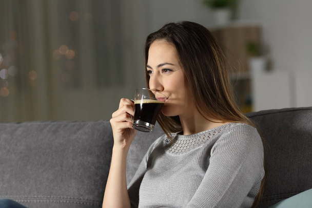 Relaxed woman drinking decaffeinated coffee in the night sitting on a couch in the living room at home - Foto, immagini