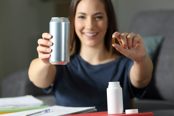 Happy student showing an energy drink tin and vitamin supplement pills at home - Foto, imagen