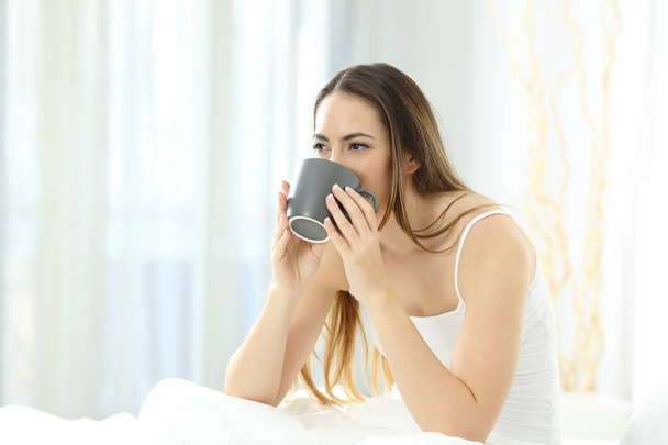Nyugodt nő felébred reggel otthon ült egy ágyon kávé, tea - Fotó, kép