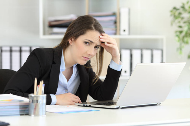 Worried office worker looking at camera sitting in a desktop - Photo, Image