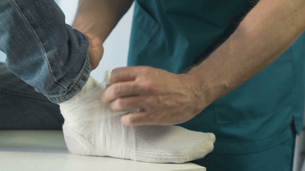 Surgeon putting cast gypsum on patients broken leg, first aid clinic, close-up - Footage, Video