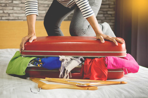 Woman trying to fit all clothing to packing her red suitcase before vacation - 写真・画像