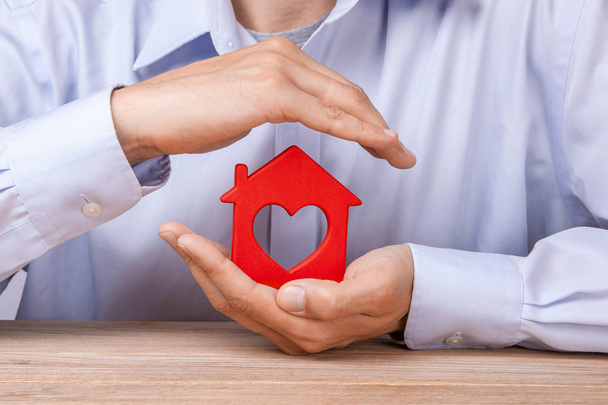Concept home insurance, protection from burglary or destruction. Man with his hands covers the houses of red color with the heart inside. - Photo, Image