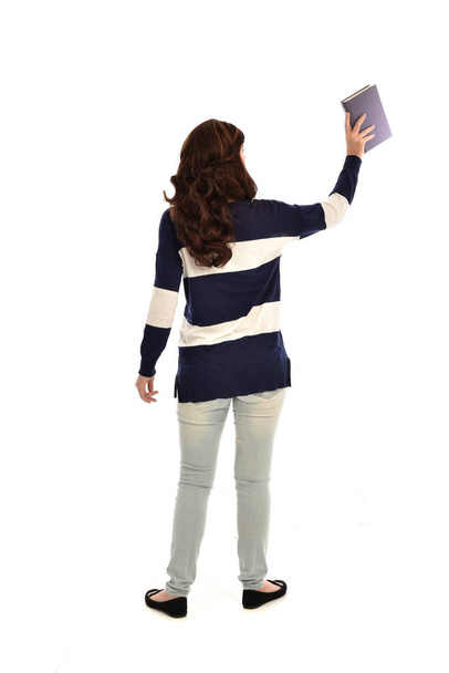 портрет дівчини в смугастому синьо-білому светрі і джинсах, що тримає книгу. стояча поза на білому фоні студії
. - Фото, зображення