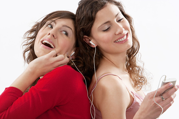 Two young women sharing their earphones to listen to music on their music player - Photo, Image