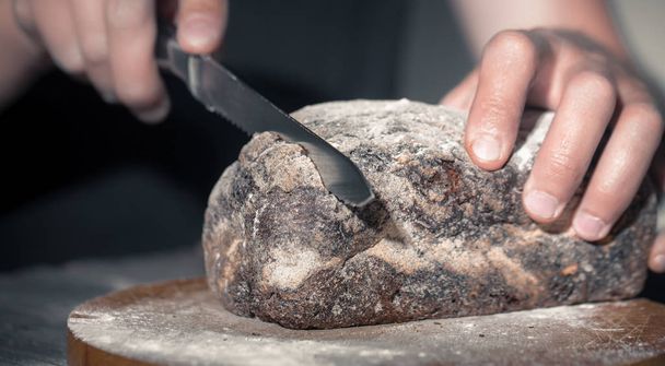 Baker snižuje čerstvý chléb na krásné dřevěné pozadí, koncept zdravých potravin a pekárna průmyslu - Fotografie, Obrázek