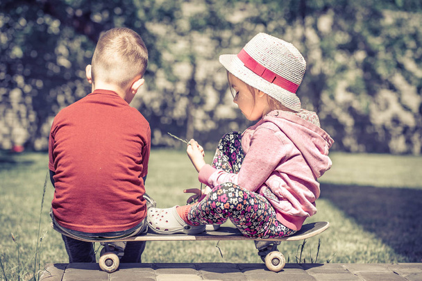 Mädchen und Junge spielen auf Skateboard, vor der Kulisse eines grünen Gartens, Konzept der Jugendfreundschaft. - Foto, Bild