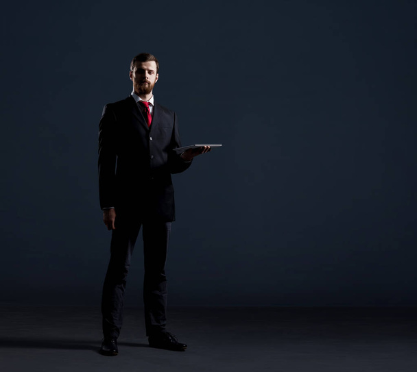 Businessman with computer tablet standing over black dramatic background. Business and office, concept. - Fotografie, Obrázek