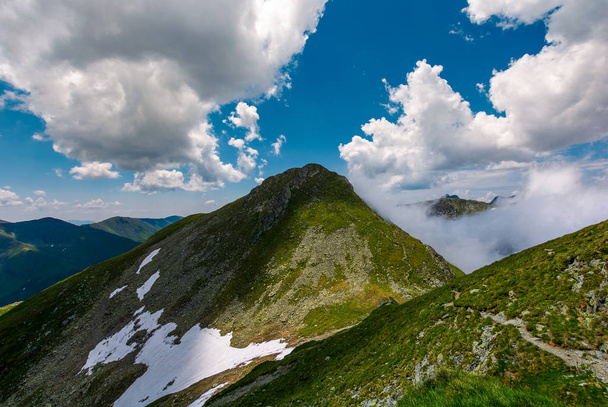 Κορυφές του την κορυφογραμμή του βουνού ανάμεσα στα σύννεφα. Πανίσχυρη σχηματισμούς με βραχώδεις κορυφές και χλοώδεις λόφους. όμορφο καλοκαιρινό τοπίο φύση σε μεγάλο υψόμετρο - Φωτογραφία, εικόνα