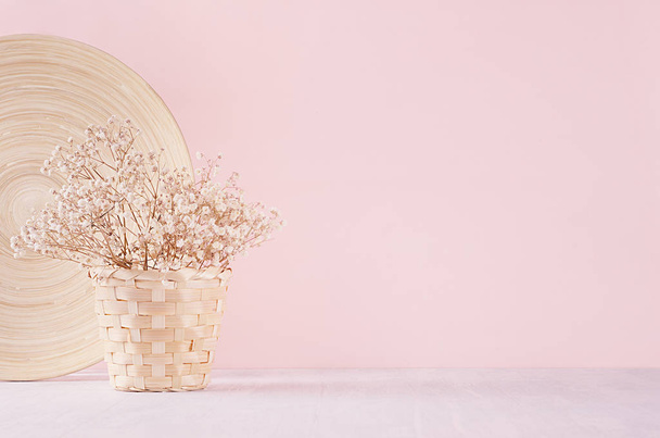 Small white dried flowers in beige wicker basket and bamboo plate on soft pink pastel background. Fresh light gentle background. - Foto, Imagen