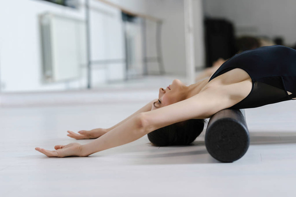 Pretty Caucasian woman doing pilates exercise on the floor with roller. - Фото, изображение