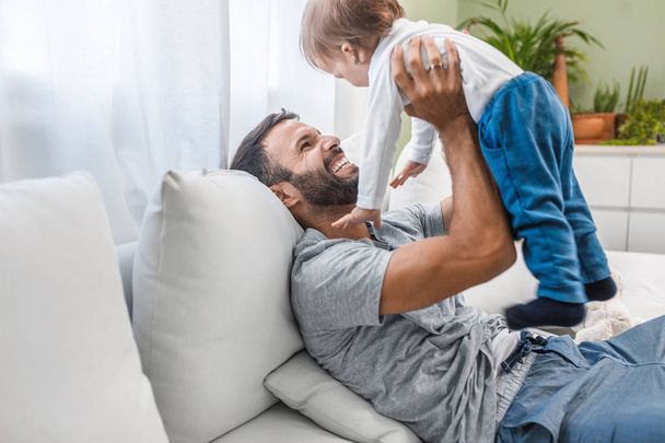 Happy handsome Caucasian man holding his cute baby son at home and laughing. - Φωτογραφία, εικόνα