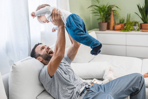 Happy handsome Caucasian man holding his cute baby son at home and laughing. - Foto, immagini