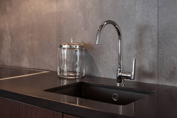 Detail einer rechteckigen Designer-Küchenspüle mit verchromtem Wasserhahn vor einer grau strukturierten Wand - Foto, Bild